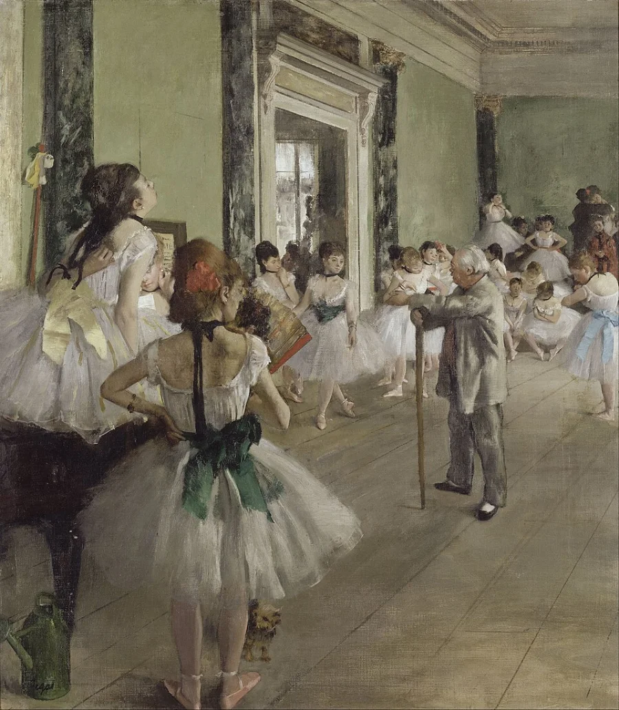 A rehearsal room seen from a high angle. Dancers wait, stretch and talk while one practises, and the figures at the edges are cut off by the sides of the picture.