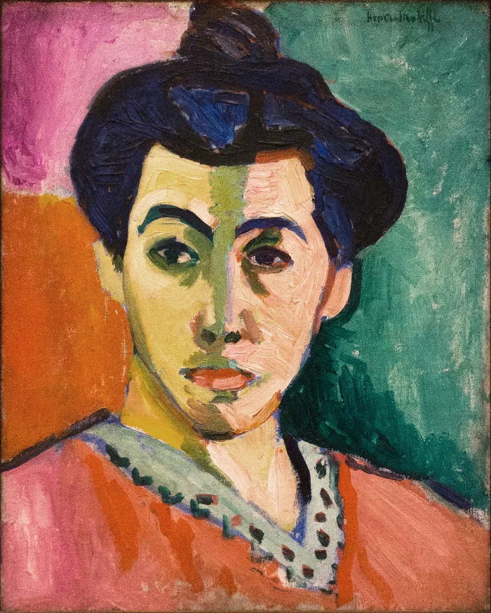A woman’s face divided down the middle by a band of green paint, with one side warm pink and the other cool, against orange and green.